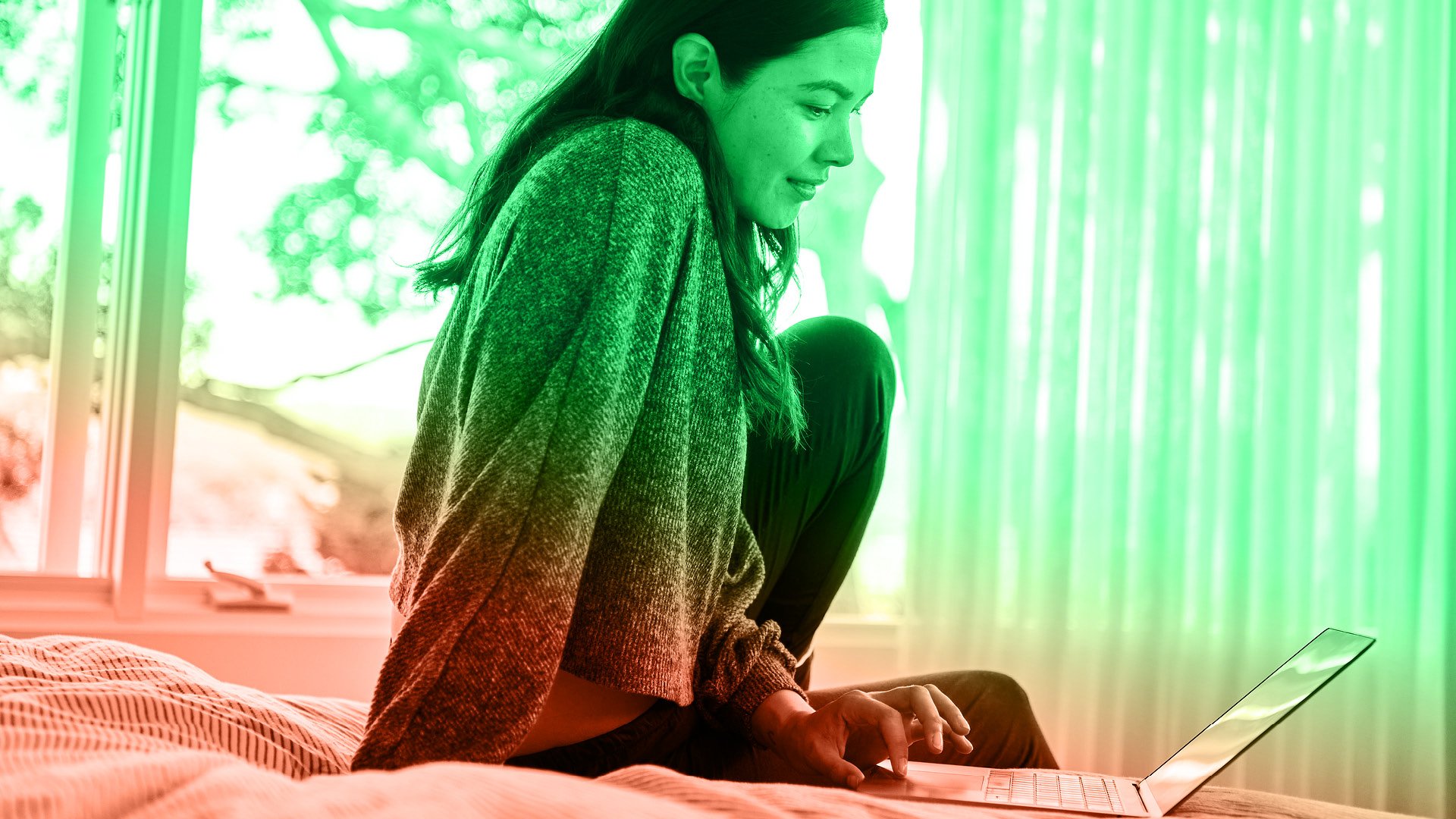 Jeune femme assise sur un lit regardant un ordinateur